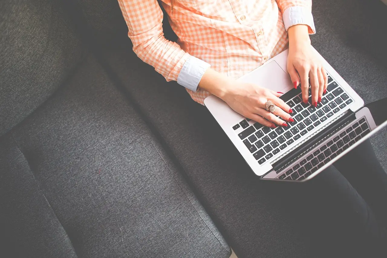 A woman typing on a laptop resting on her lap on a gray couch