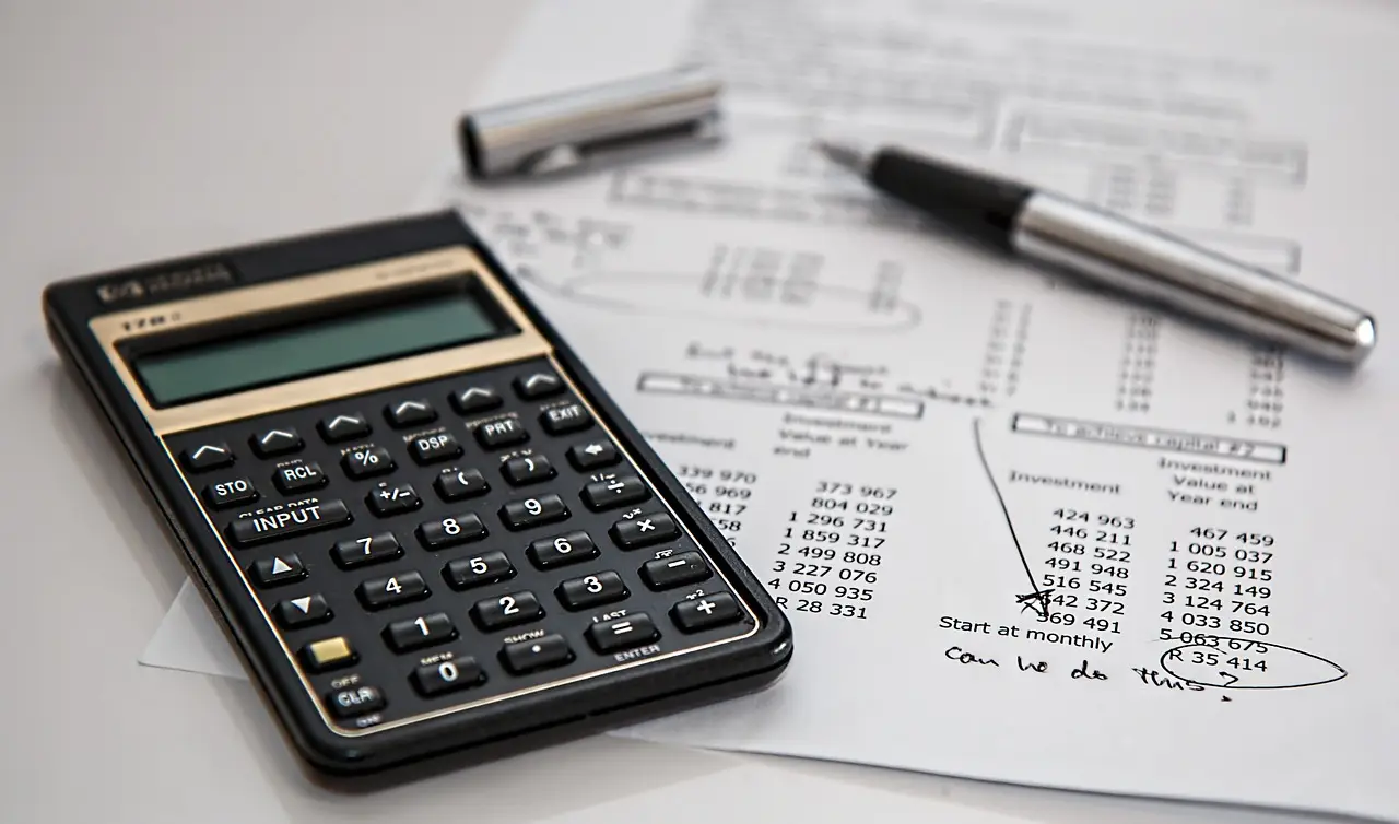 A calculator and pen resting on a printed financial spreadsheet full of numbers