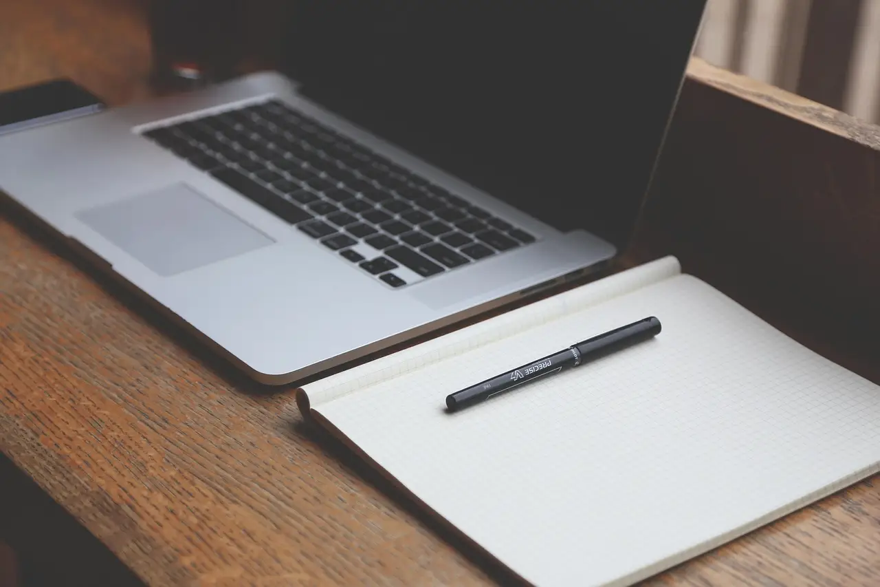 A person checking email on a laptop at an office desk, a coffee cup beside the keyboard